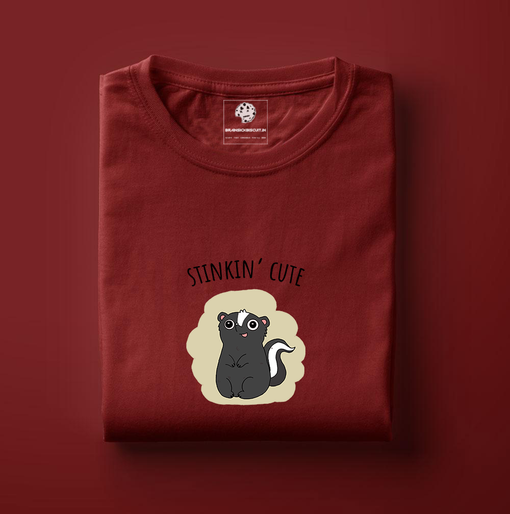 cute black skunk with stinkin cute on folded maroon t-shirt.