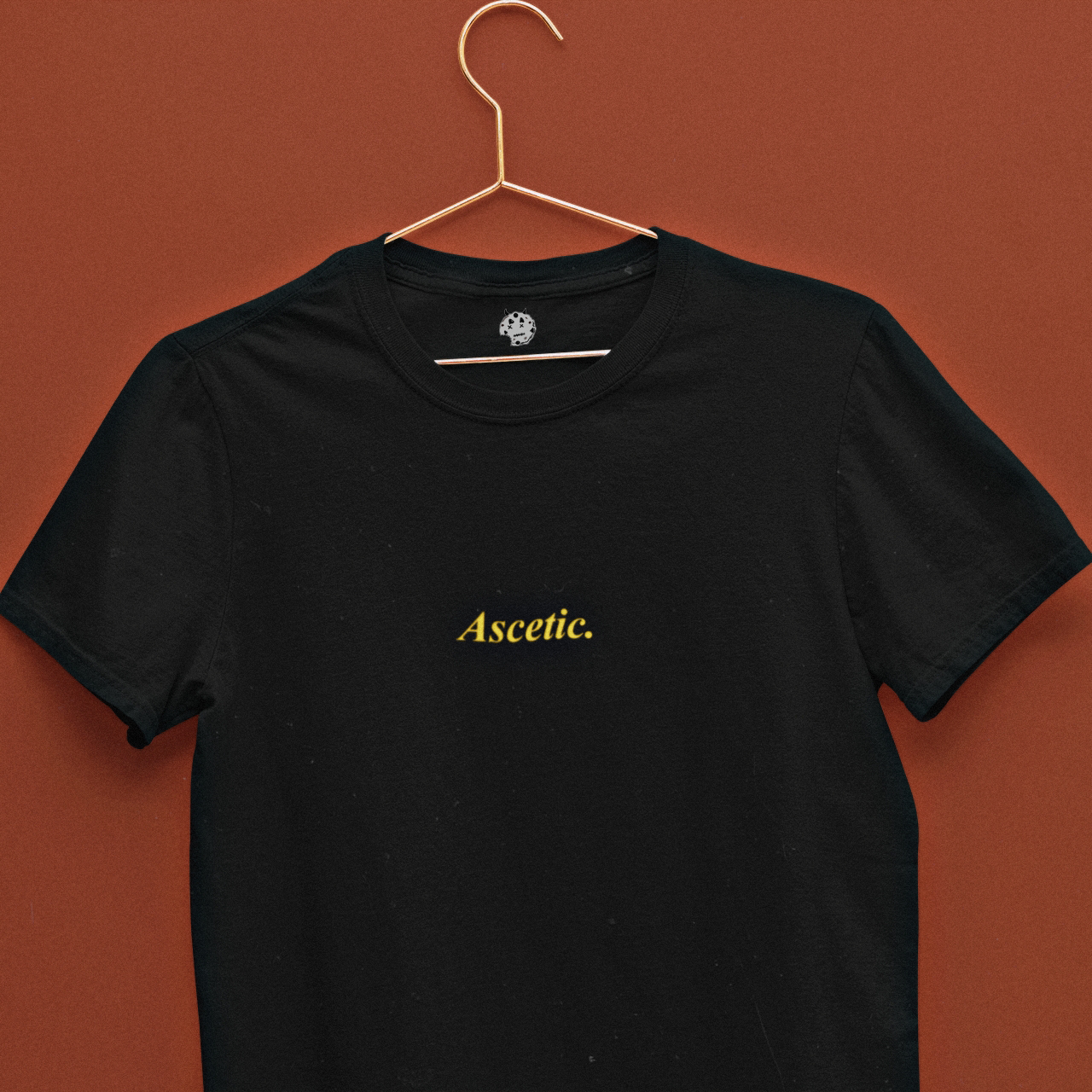 Ascetic written in golden yellow on black t-shirt on a hanger.