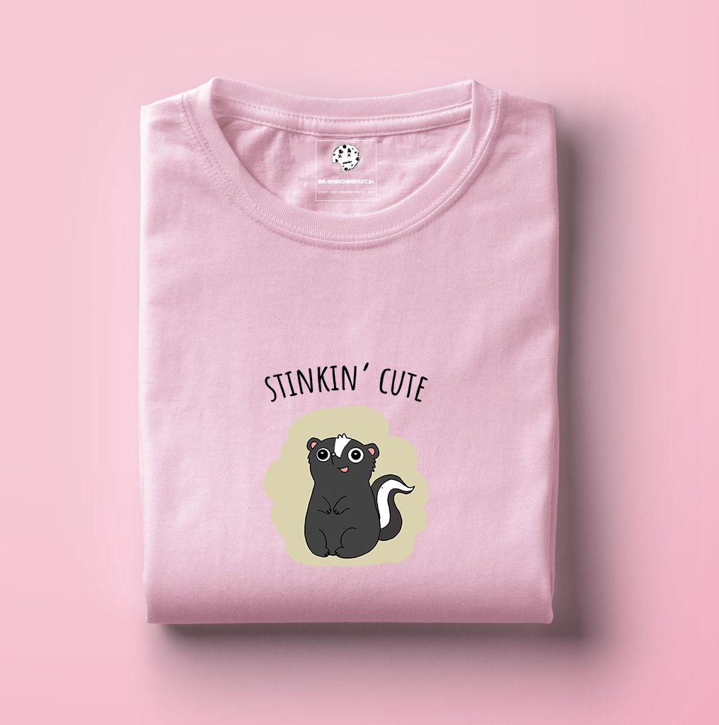 cute black skunk with stinkin cute on folded light baby pink t-shirt.